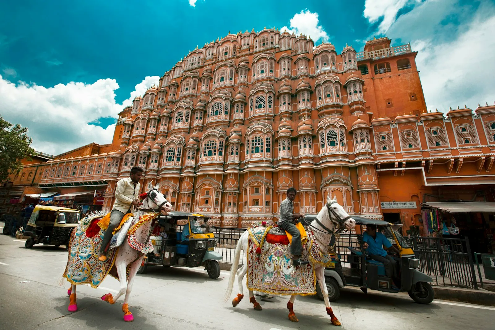 Decorated horses passing the pink facade of the Hawa Mahal in Jaipur, Rajasthan