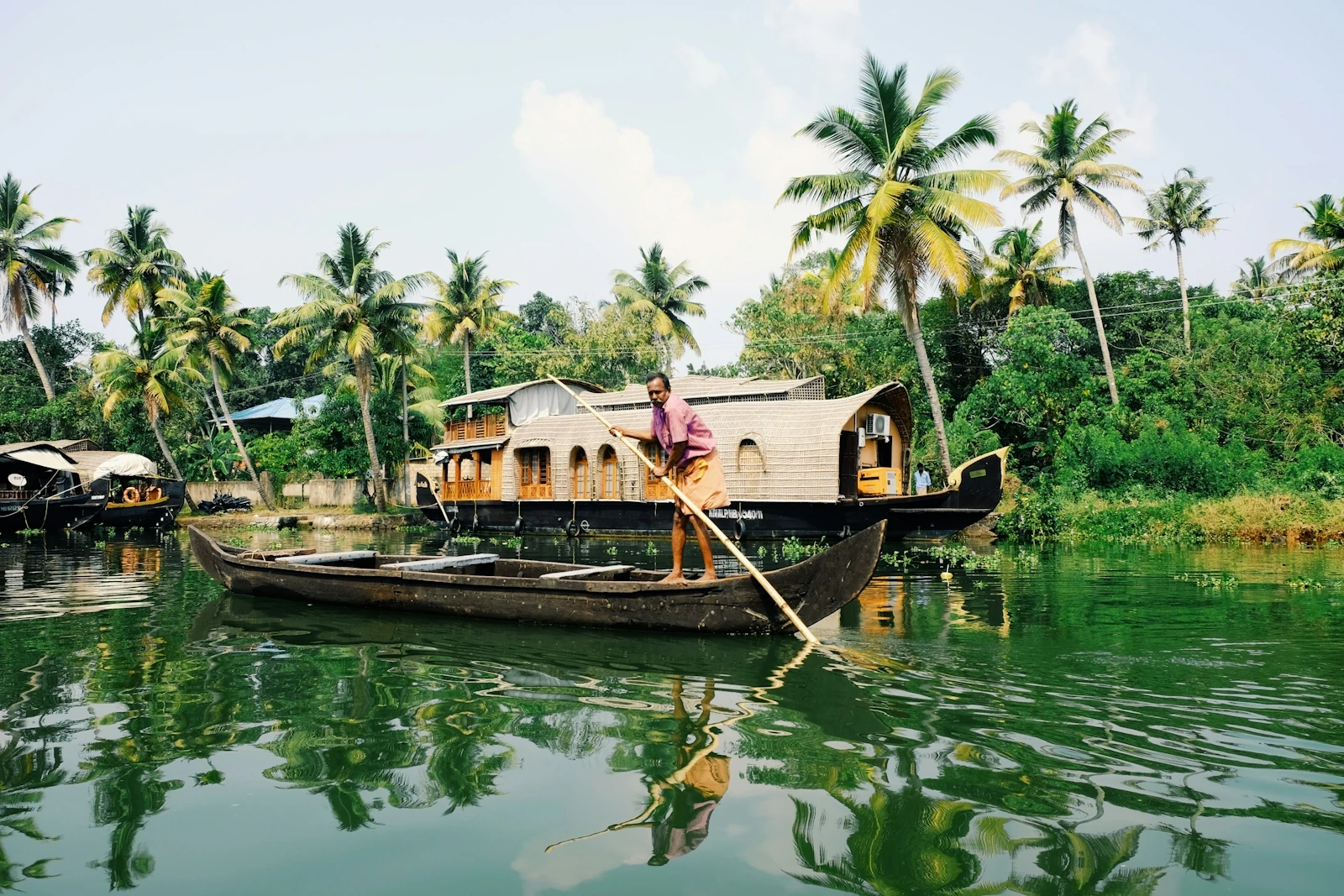 A boatman poling a small wooden canoe along a calm Kerala backwater