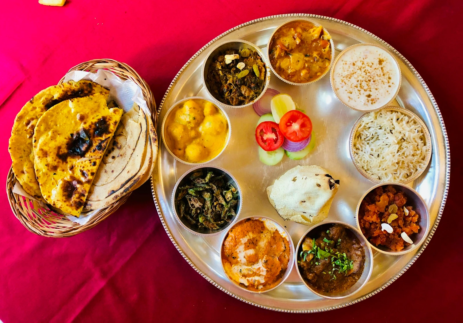 An Indian thali on a stainless steel tray, with rice, several curries, bread, pickle and a sweet