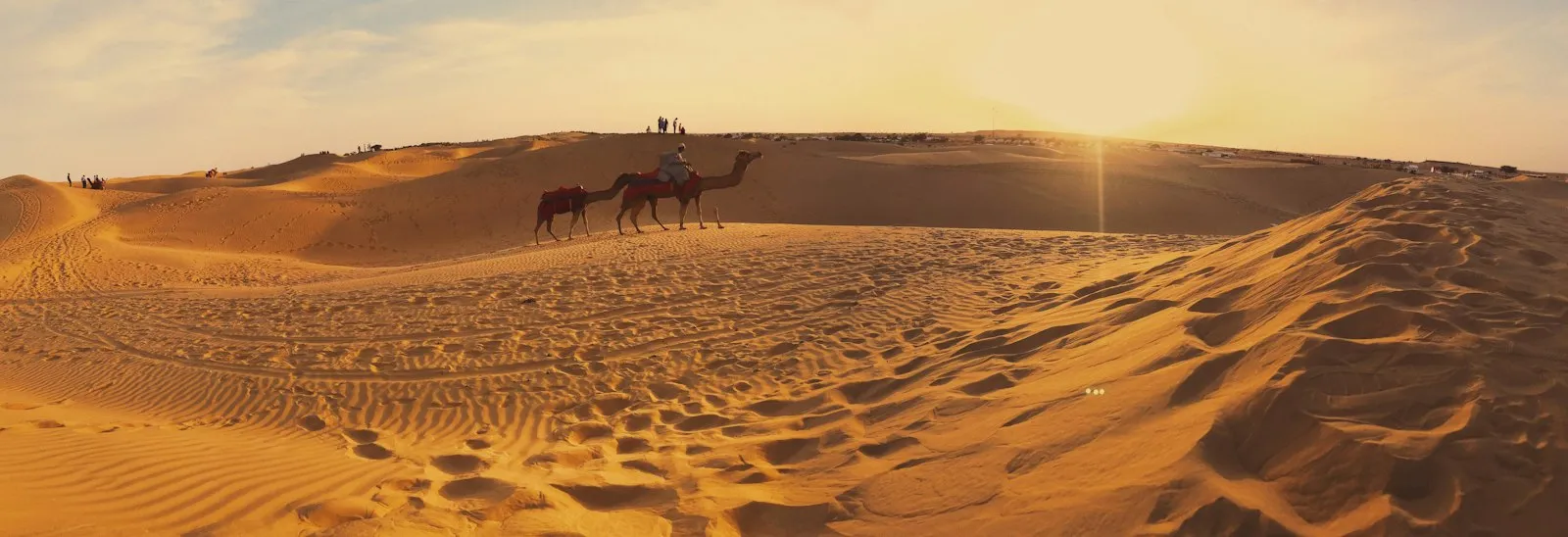Travellers riding camels across the golden dunes of the Thar Desert near Jaisalmer, Rajasthan, at dusk