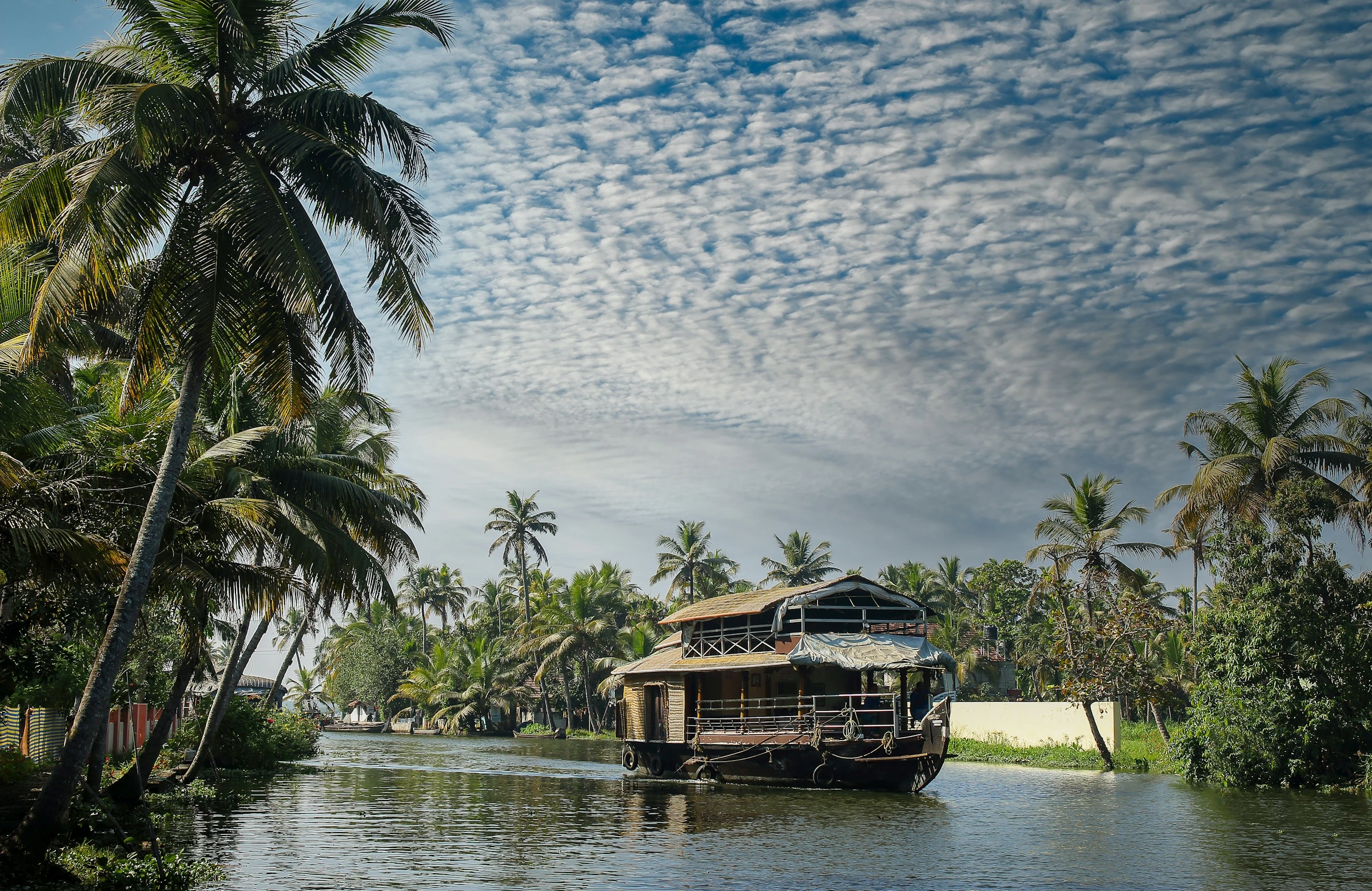 A traditional wooden kettuvallam houseboat moored beside palm trees on a Kerala backwater canal