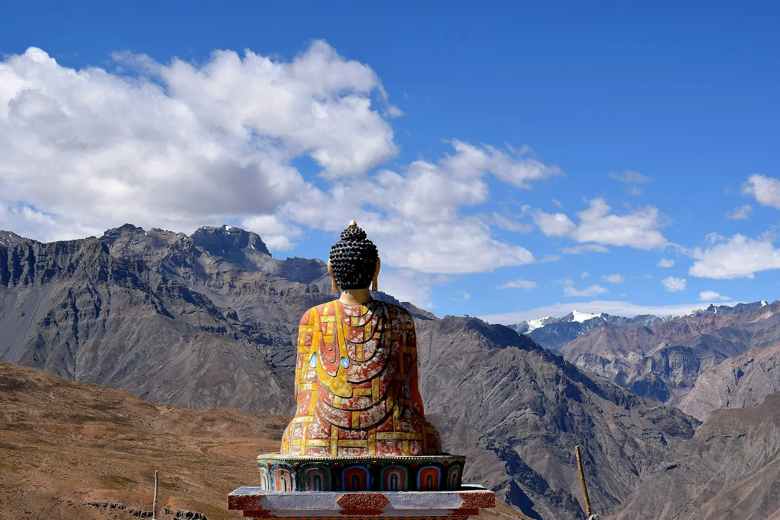 A large hillside Buddha statue at Langza gazing over the bare mountains of Spiti Valley under a bright blue sky