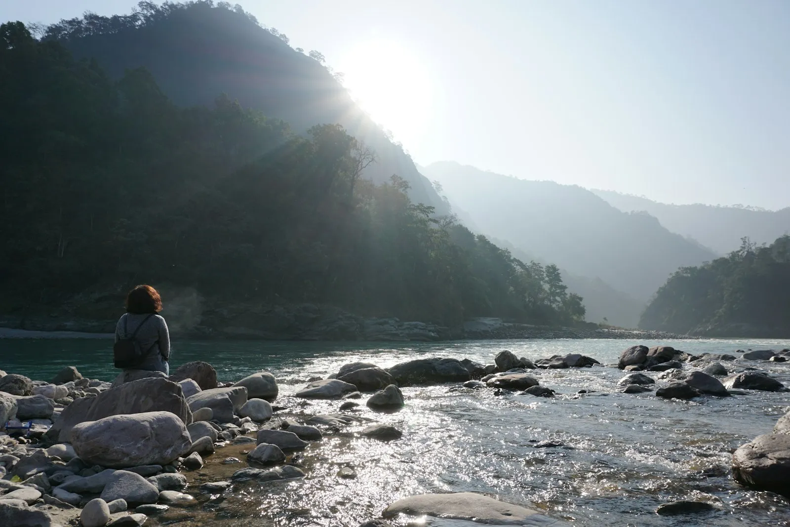 A traveller sitting quietly on a rock beside a river in the Himalayan foothills