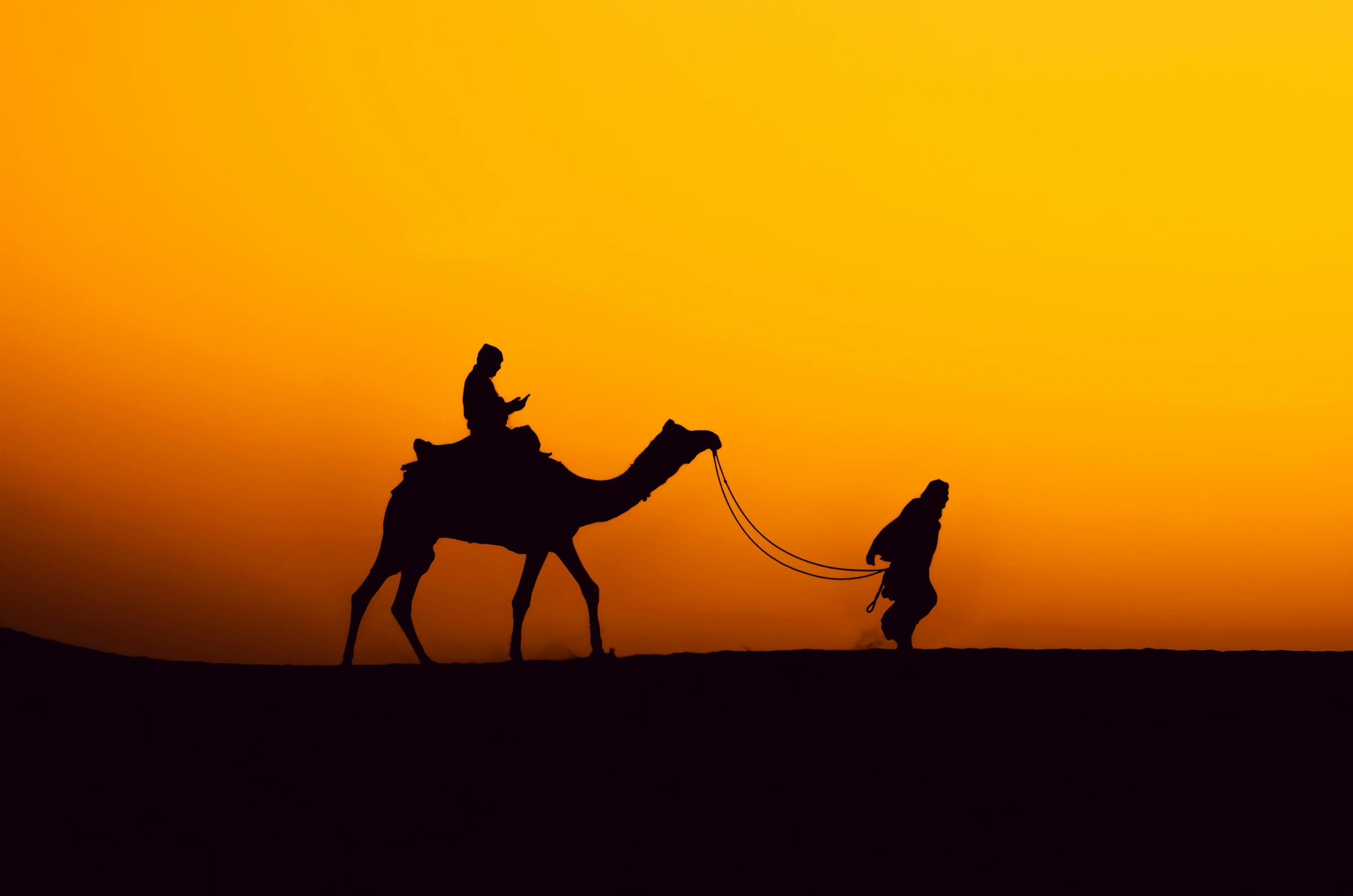 A lone camel rider crossing the Thar Desert dunes near Jaisalmer, Rajasthan, at sunset