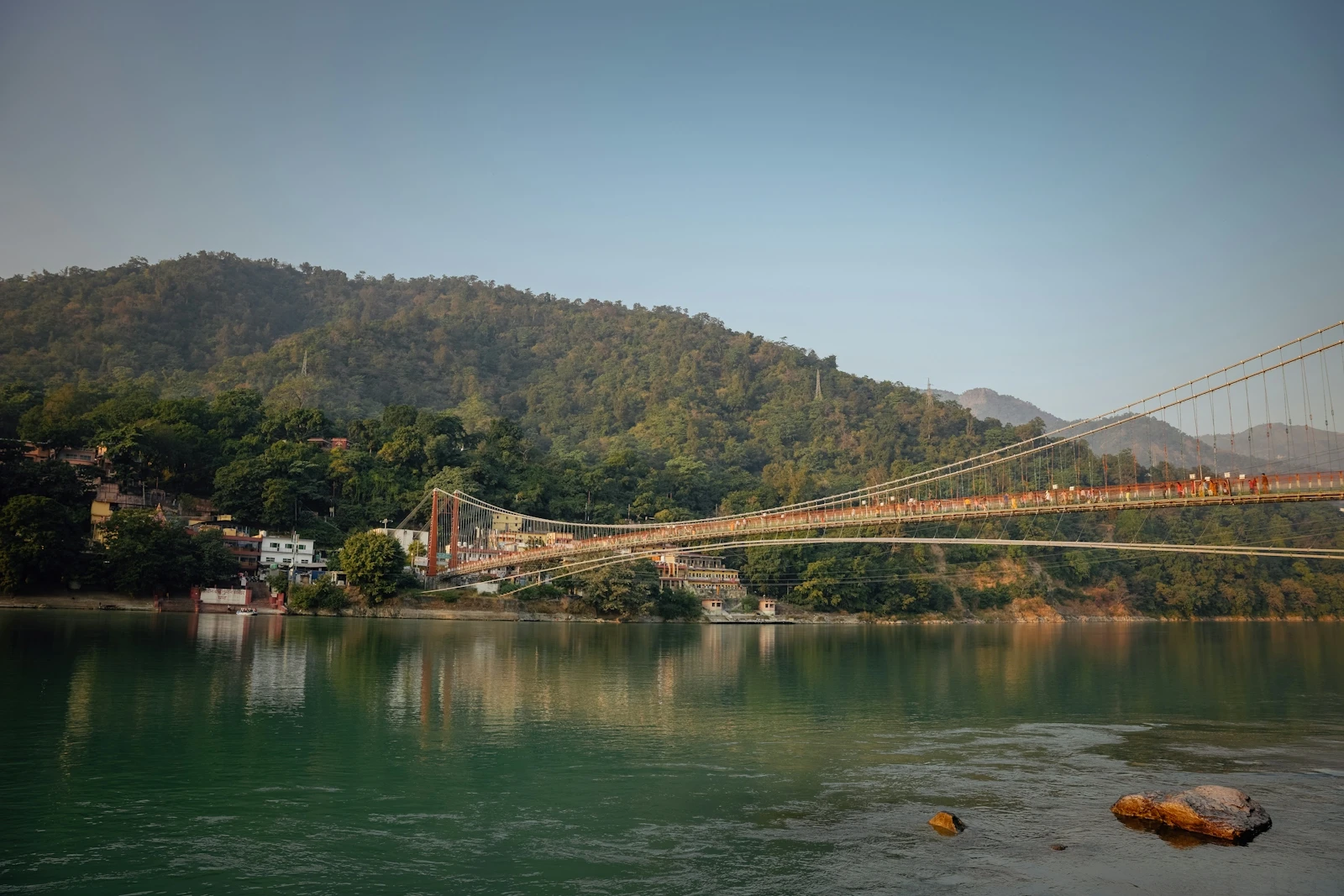 A footbridge over the river Ganga below forested hills at Rishikesh in the Himalayan foothills