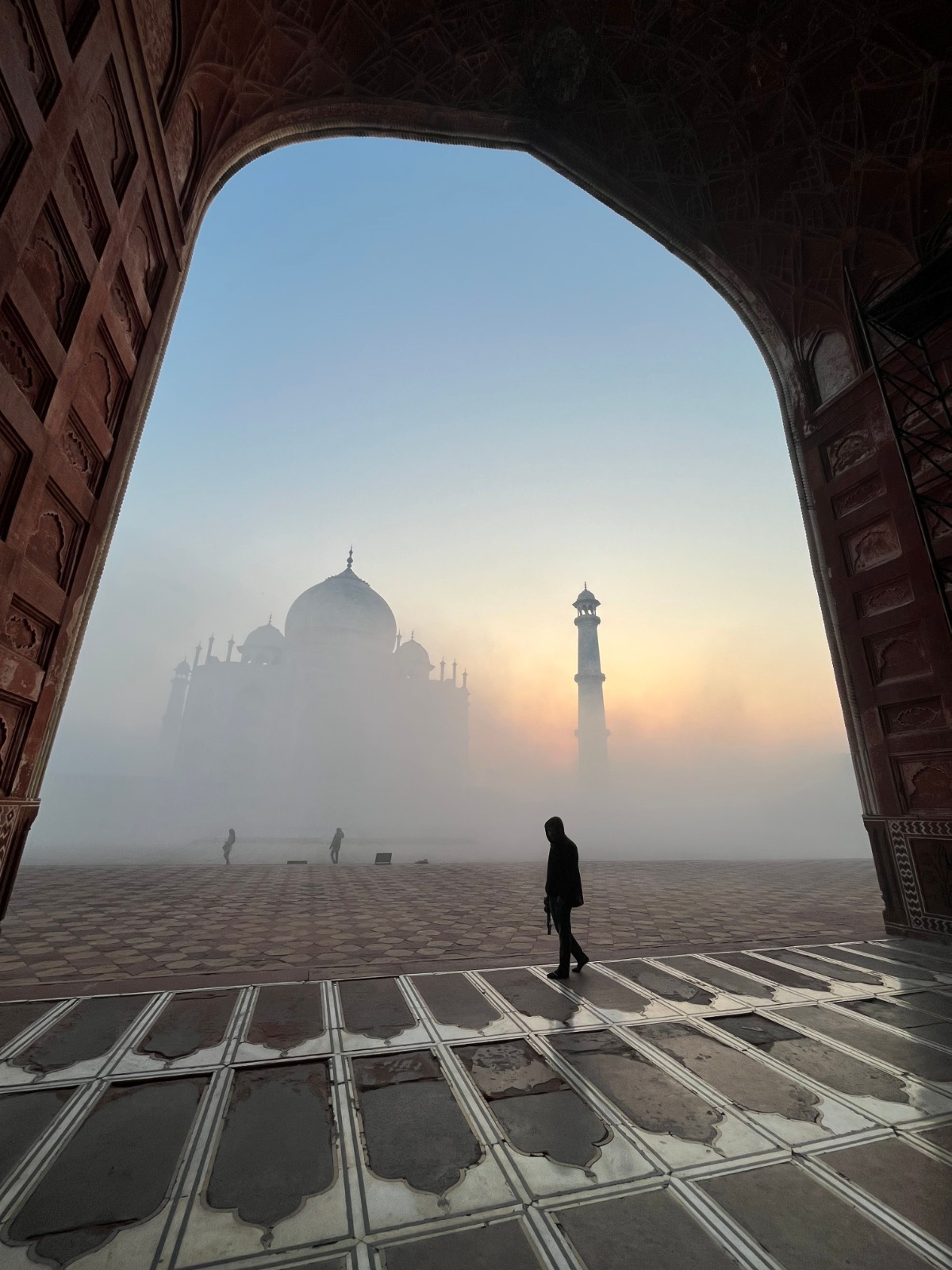 The Taj Mahal emerging from early morning mist, a lone figure in the foreground
