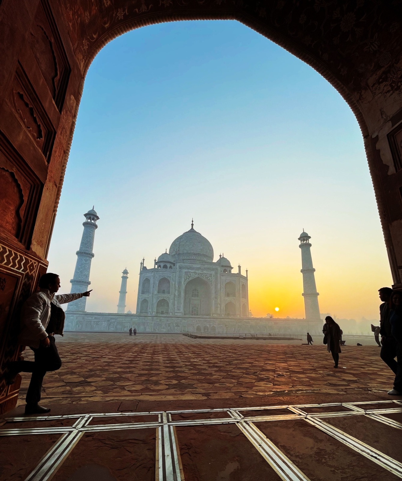 A guide pointing at the Taj Mahal at sunrise, very few people in the complex